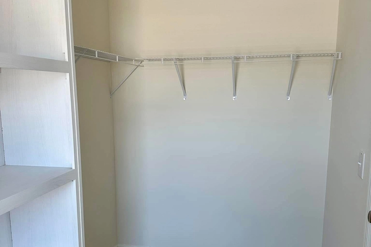 Empty walk-in closet with beige walls, a white shelving unit on the left, and a white wire shelf with brackets on the right wall.