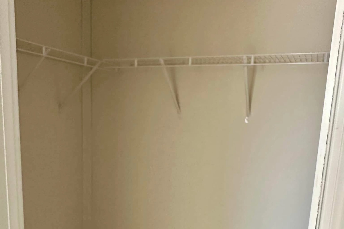 Empty closet with beige walls and a white wire shelf mounted on the back and side walls.