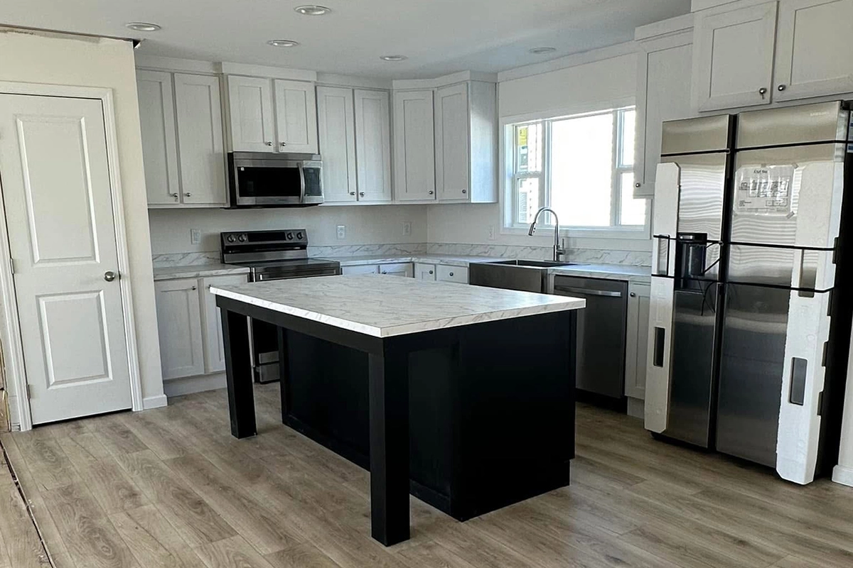 Modern kitchen with white cabinets, stainless steel appliances, a marble-topped island with black base, wood-look flooring, and a large refrigerator.