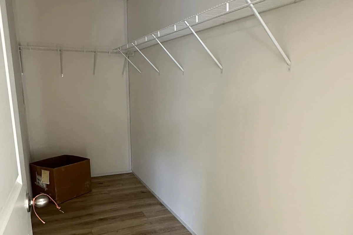 An empty walk-in closet with white wire shelving and a brown cardboard box on a wooden floor near the back wall.
