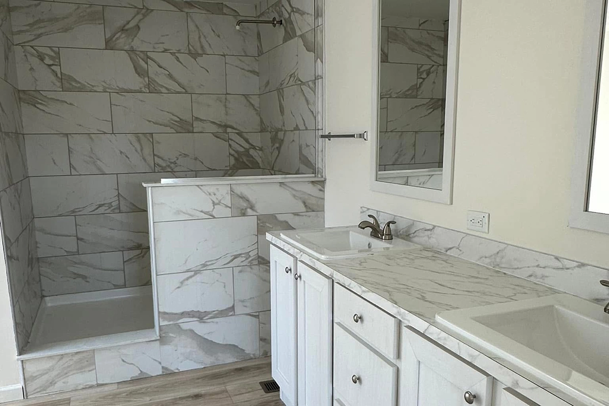 Modern bathroom with dual sinks, white cabinets, marble countertops, and a walk-in shower with tiled walls and a half wall divider.