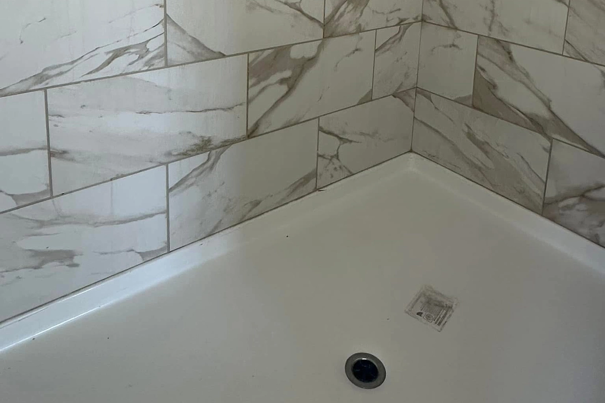 White bathtub with a central drain, surrounded by walls covered in marble-patterned tiles arranged in a staggered pattern.