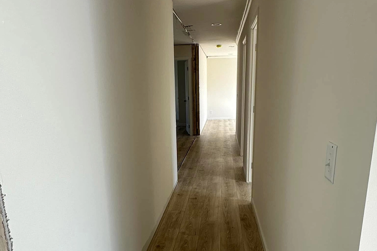 A hallway with light-colored walls and wood flooring, featuring several doorways on the right and an open space visible at the end.