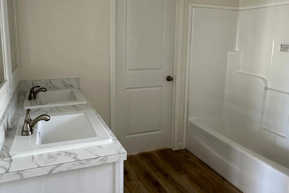 A bathroom with double sinks, marble countertops, a white bathtub with shower, and wood-look flooring.