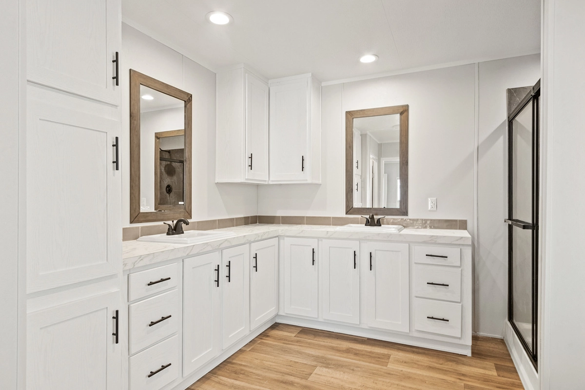 Modern bathroom with white cabinets and countertops, two mirrors, dual sinks, black fixtures, and wood-style flooring.