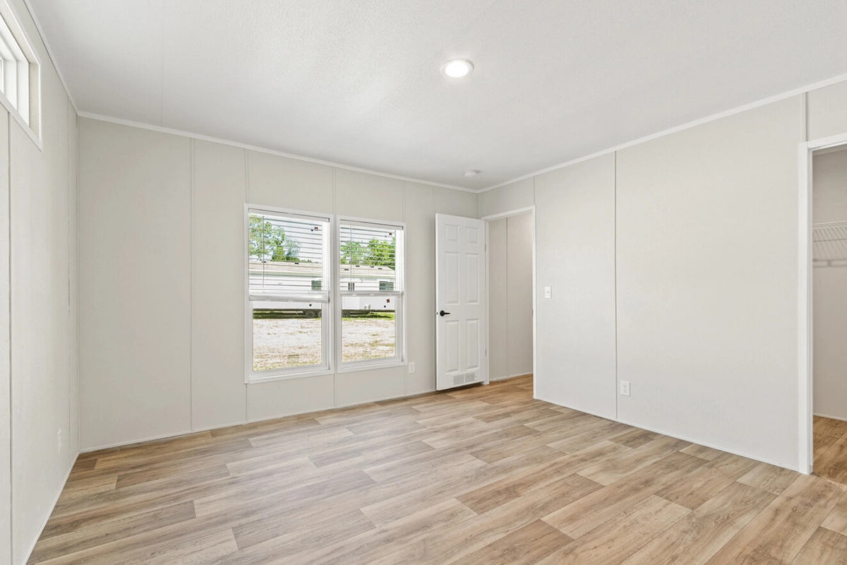 Empty room with light-colored walls, two windows, a white door, and wood-patterned flooring; closet door open on the right side.