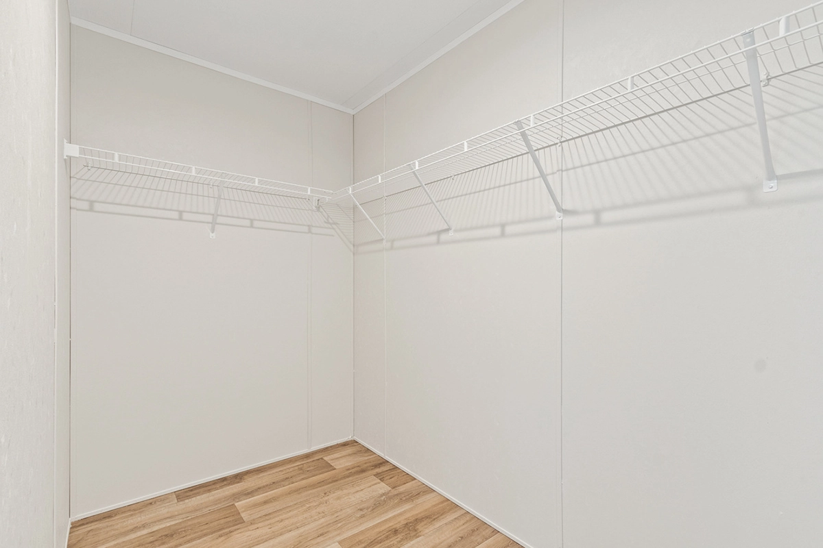 Empty walk-in closet with beige walls, wooden floor, and white wire shelving along two walls.