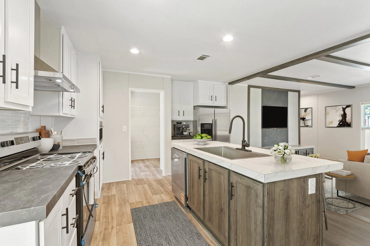 Modern kitchen with white cabinets, stainless steel appliances, a central island with a sink, and an open view into a living area with a wall-mounted TV and artwork.