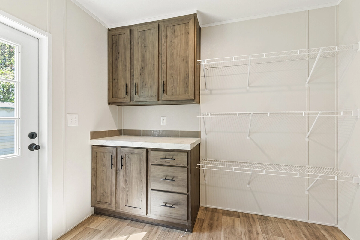 Laundry room with wood cabinets, a countertop, and white wire shelving on the wall. Door with window on the left, light wood flooring, and neutral-colored walls.