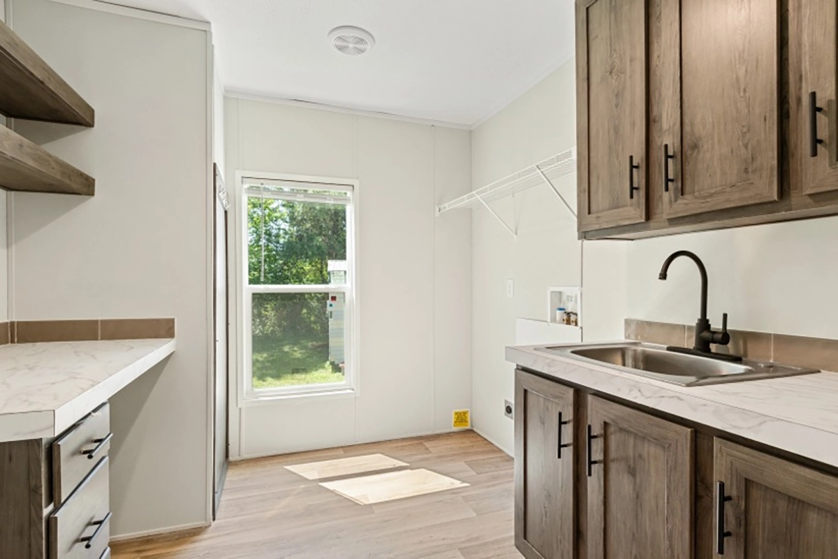 Laundry room with wood cabinets, a sink, open shelves, a large window, and a wire shelf above a washer and dryer hookup.