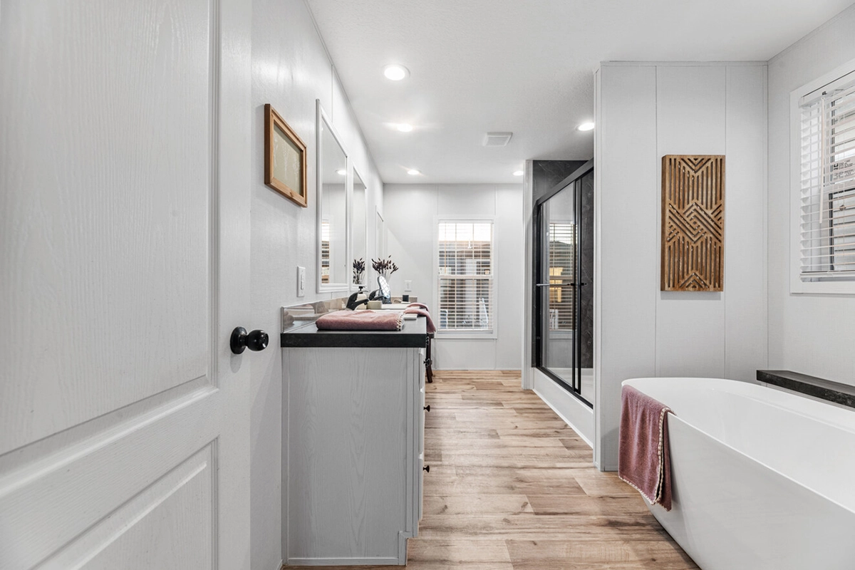 Modern bathroom with wood-style flooring, a freestanding tub with a pink towel, double sinks, large mirrors, and a glass-enclosed shower.