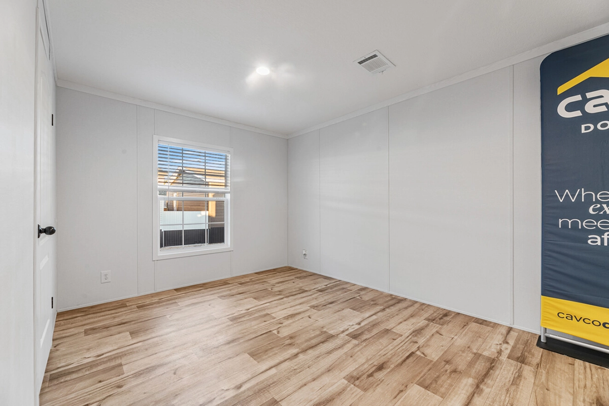Empty room with light wood flooring, white walls, a window with blinds, ceiling light, and a partial view of a promotional banner on the right.