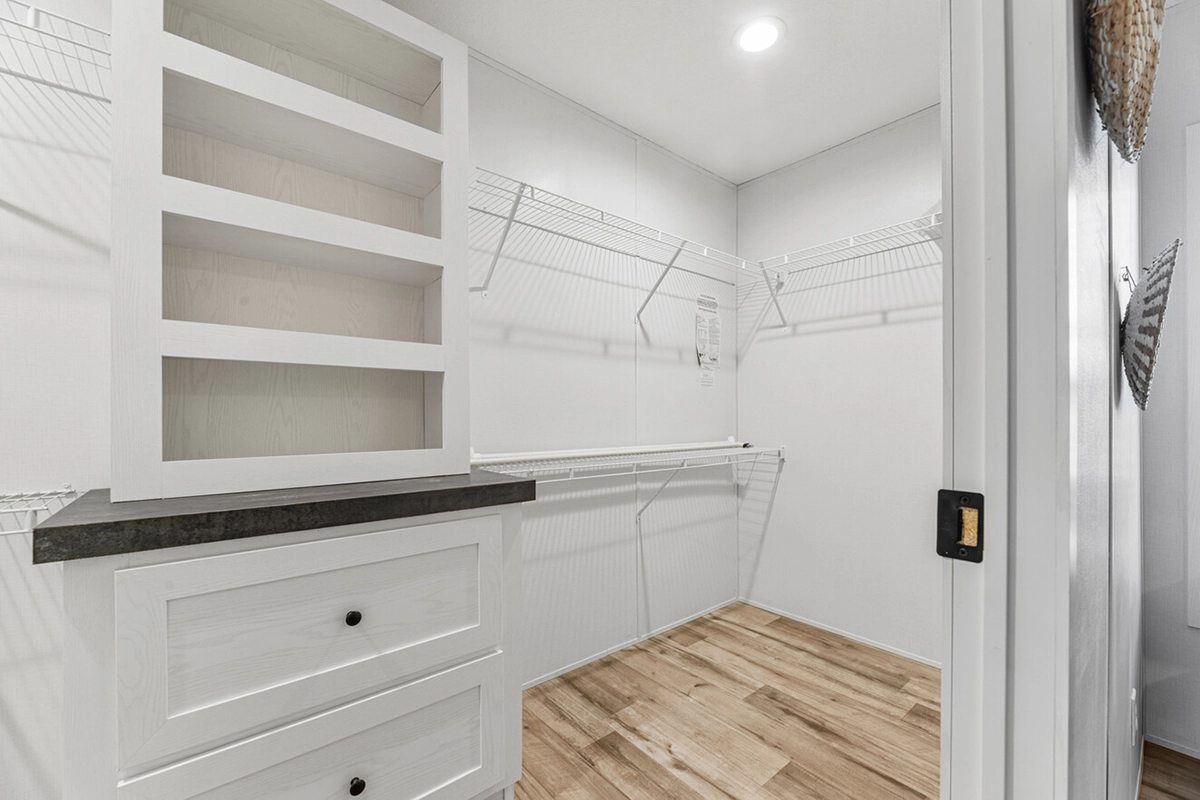 Empty walk-in closet with white shelves, built-in drawers, wire racks along the walls, light wood flooring, and recessed ceiling lighting.