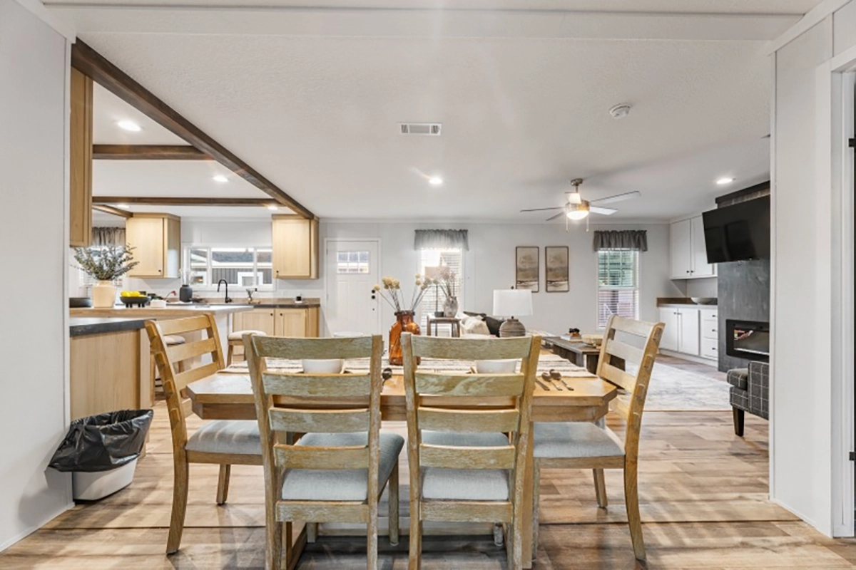 A dining table with six wooden chairs sits in an open-plan kitchen and living area with wood flooring and neutral-colored decor.