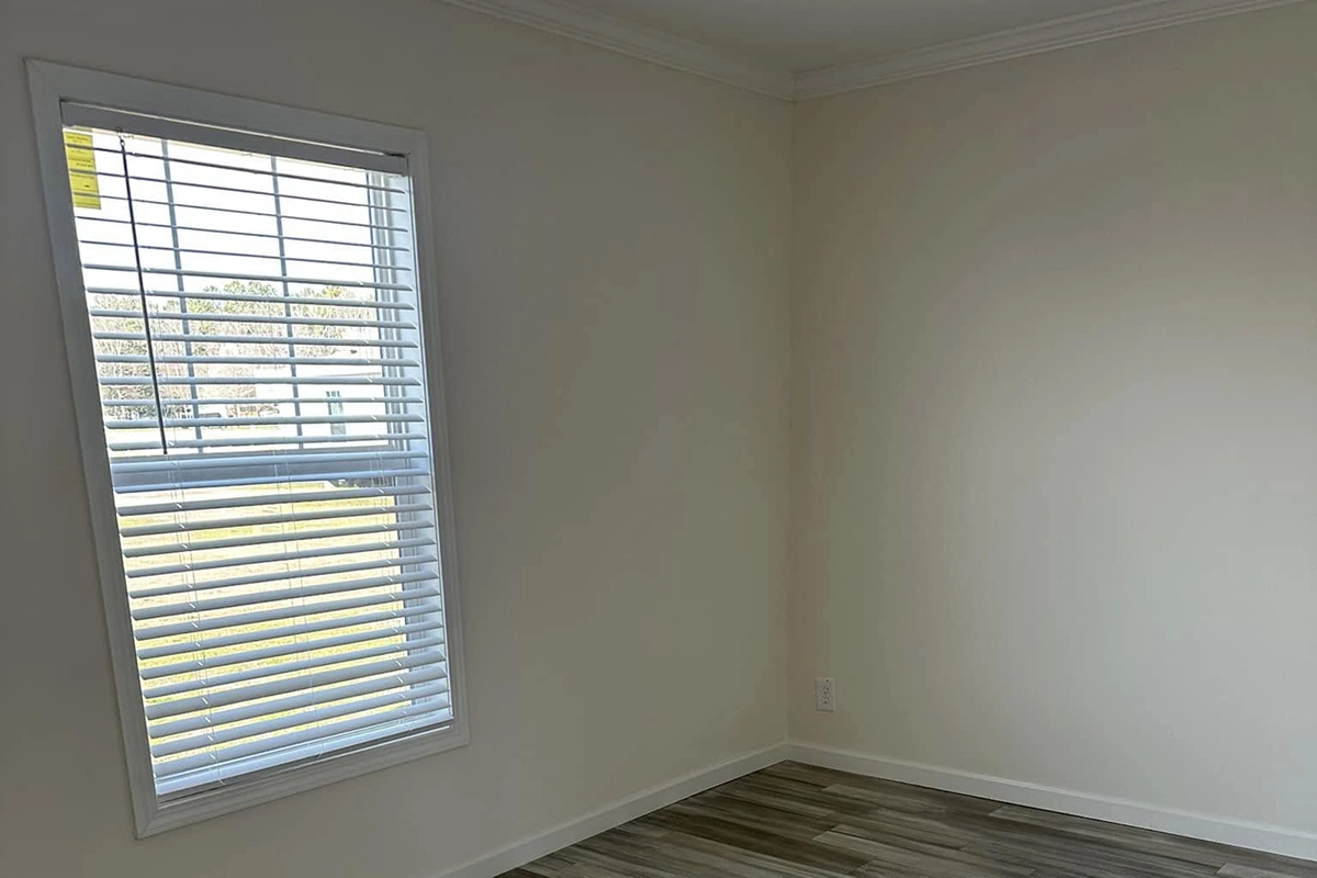 An empty room with white walls, a window with blinds partially open, and wood-patterned vinyl flooring.