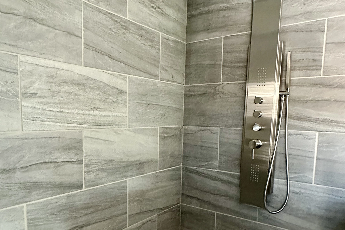IMG_6392 copy Shower with large gray stone tiles and a modern stainless steel panel featuring knobs, a handheld showerhead, and water jets.
