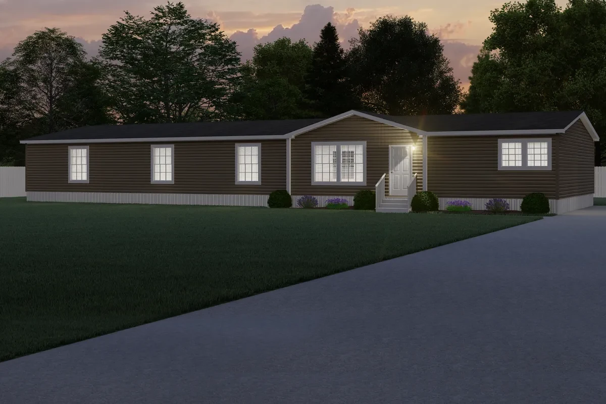 A single-story brown manufactured home with white trim, lit windows, front steps, and a paved driveway, set against trees at dusk.
