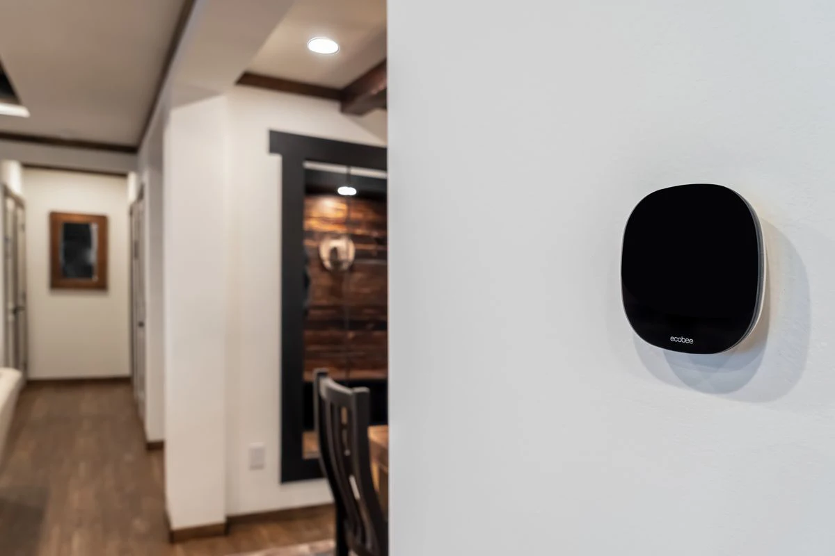 04e33f52-99f5-437c-bd75-605d10d7a614 A smart thermostat is mounted on a white wall in a modern home hallway with wood floors and contemporary decor.
