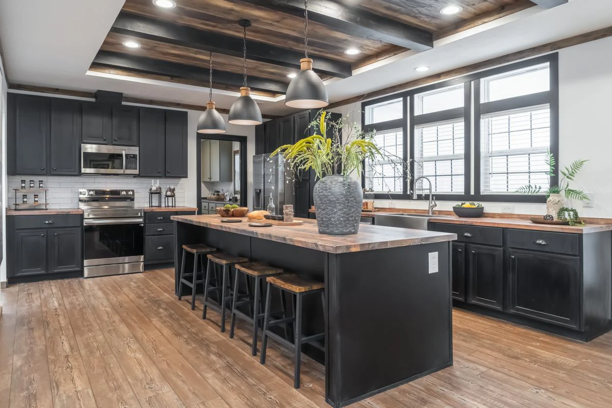 05edd356-2219-4a95-93d1-9c9e4fa9f783 Modern kitchen with black cabinets, wood countertops, stainless steel appliances, a large island with bar stools, pendant lights, and potted plants.