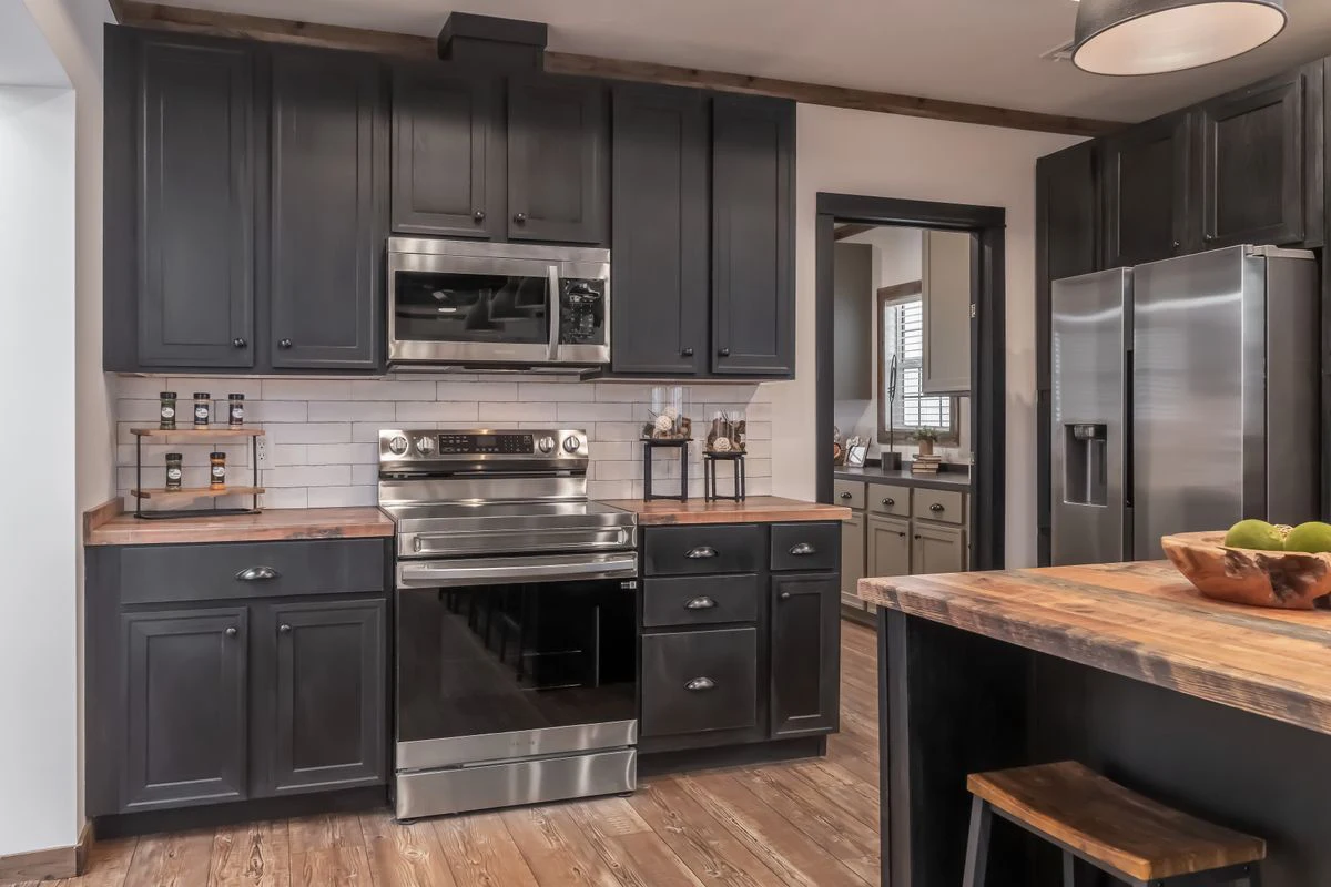 10209999-38a6-4dbf-9d19-69e068414f42 Modern kitchen with dark cabinets, stainless steel appliances, white subway tile backsplash, wooden countertops, and hardwood flooring.