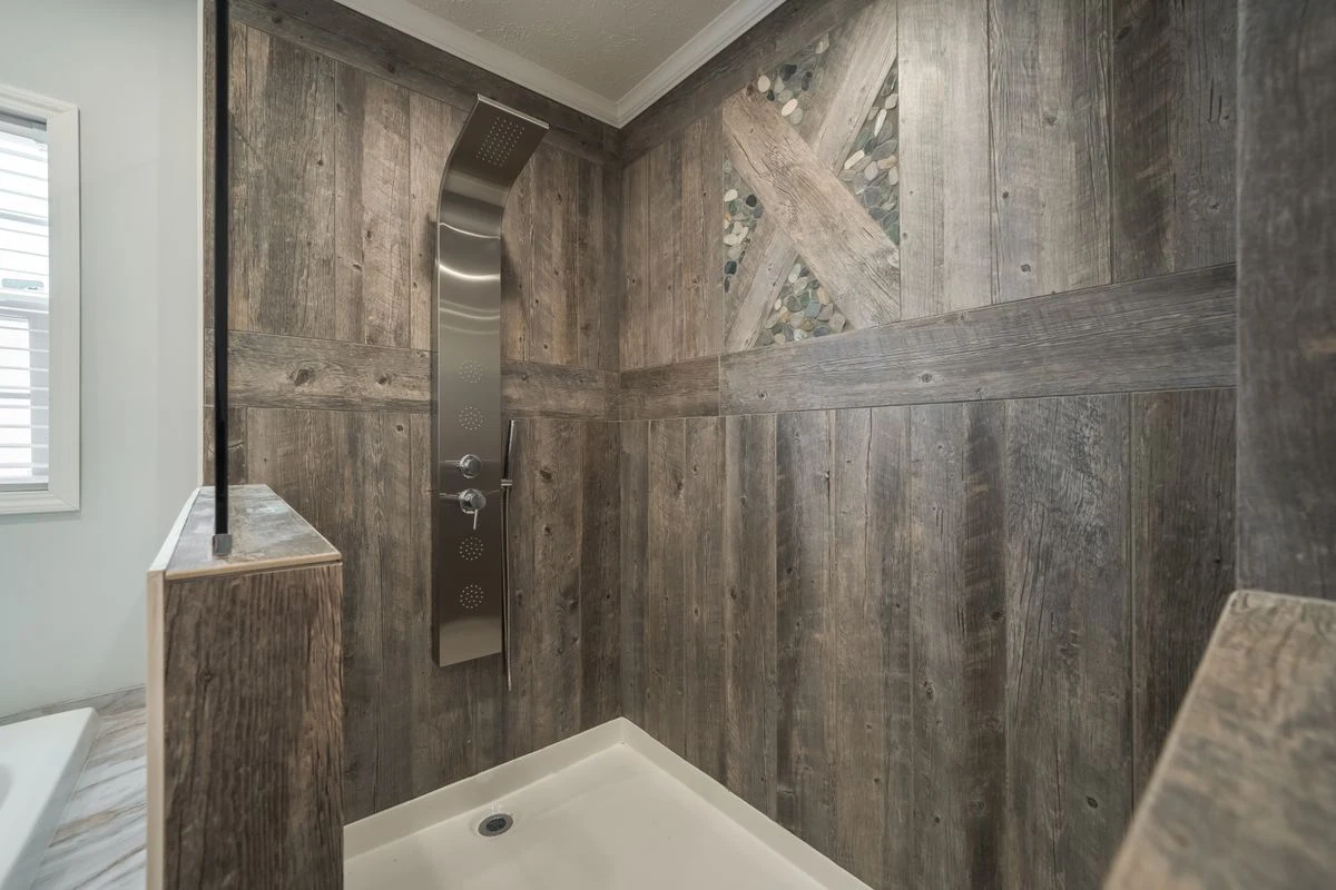 Shower with weathered wood-look walls, a modern stainless steel shower panel, pebble accent inlay, and a white shower base.