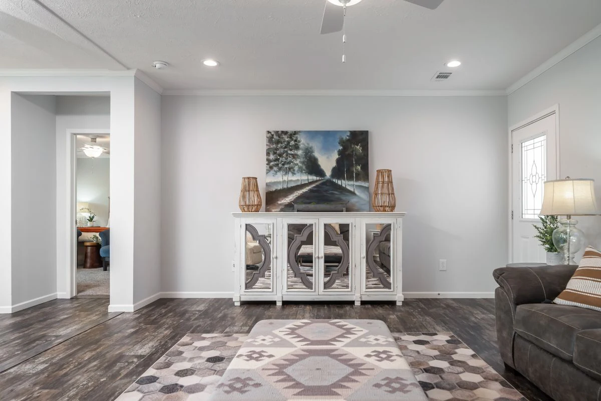 A living room with a geometric rug, mirrored console table, two lamps, a landscape painting, and neutral-colored walls and flooring.