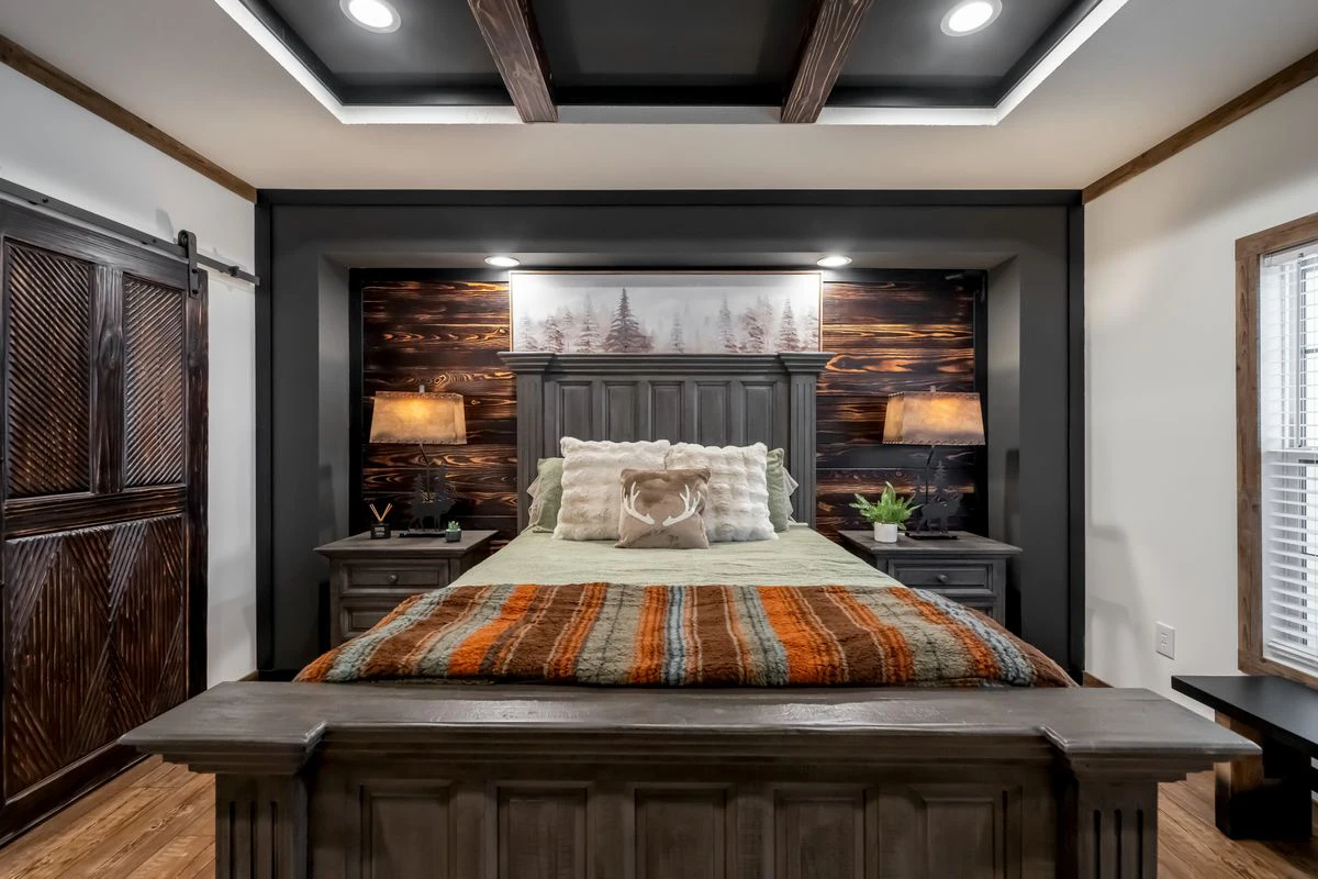 501c5605-c924-4e49-b288-052dfb151ca5 A rustic bedroom features a wooden bed with striped bedding, matching nightstands with lamps, a wood accent wall with art, and a large window letting in natural light.