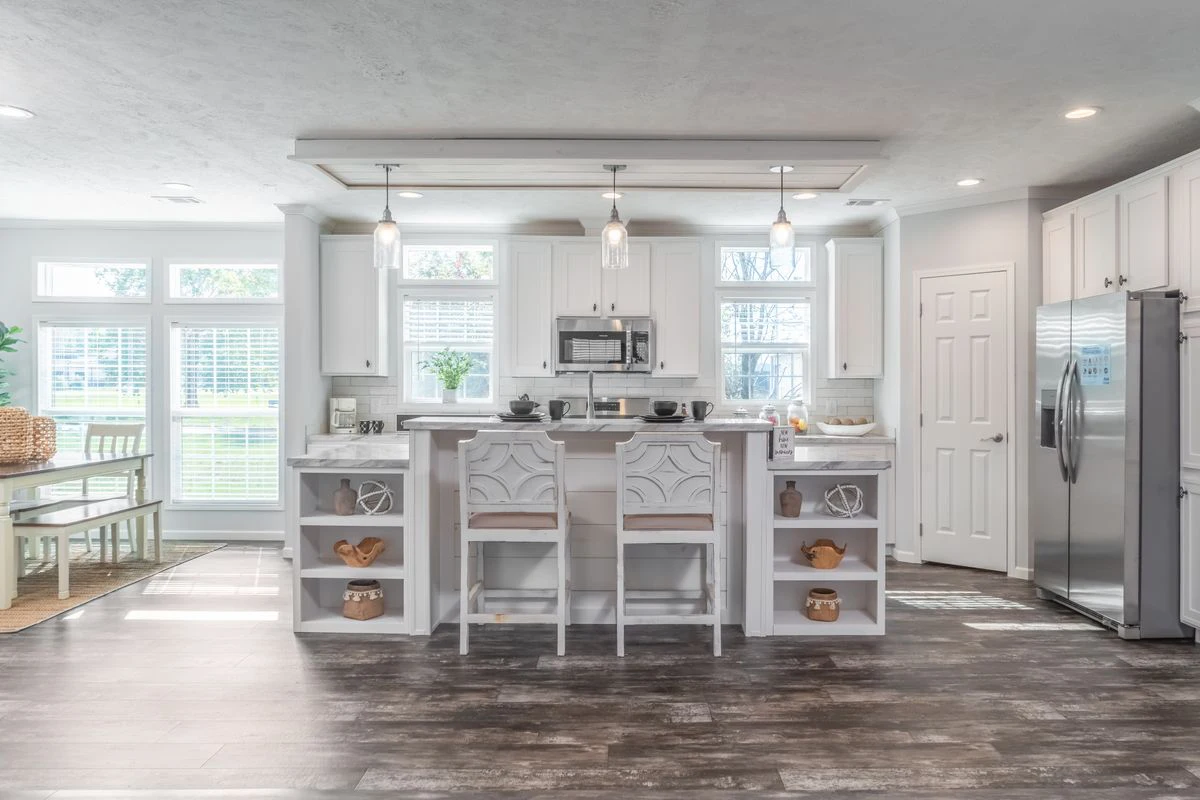 Modern kitchen with white cabinets, stainless steel appliances, a center island with three chairs, open shelves, pendant lights, and large windows providing natural light.