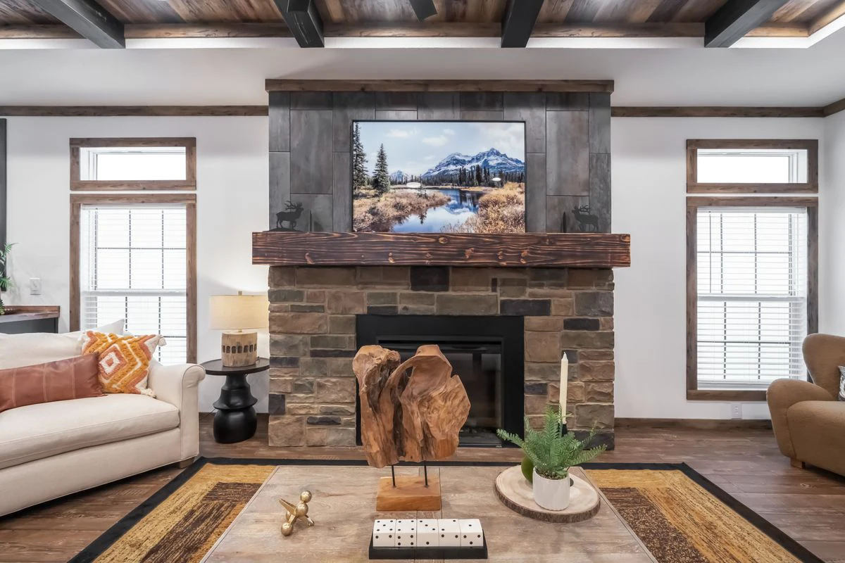 65b9e300-4541-4c65-8480-0315826a09b6 A living room with a stone fireplace, mounted TV, rustic wood accents, neutral sofas, and decorative items on a wooden coffee table.