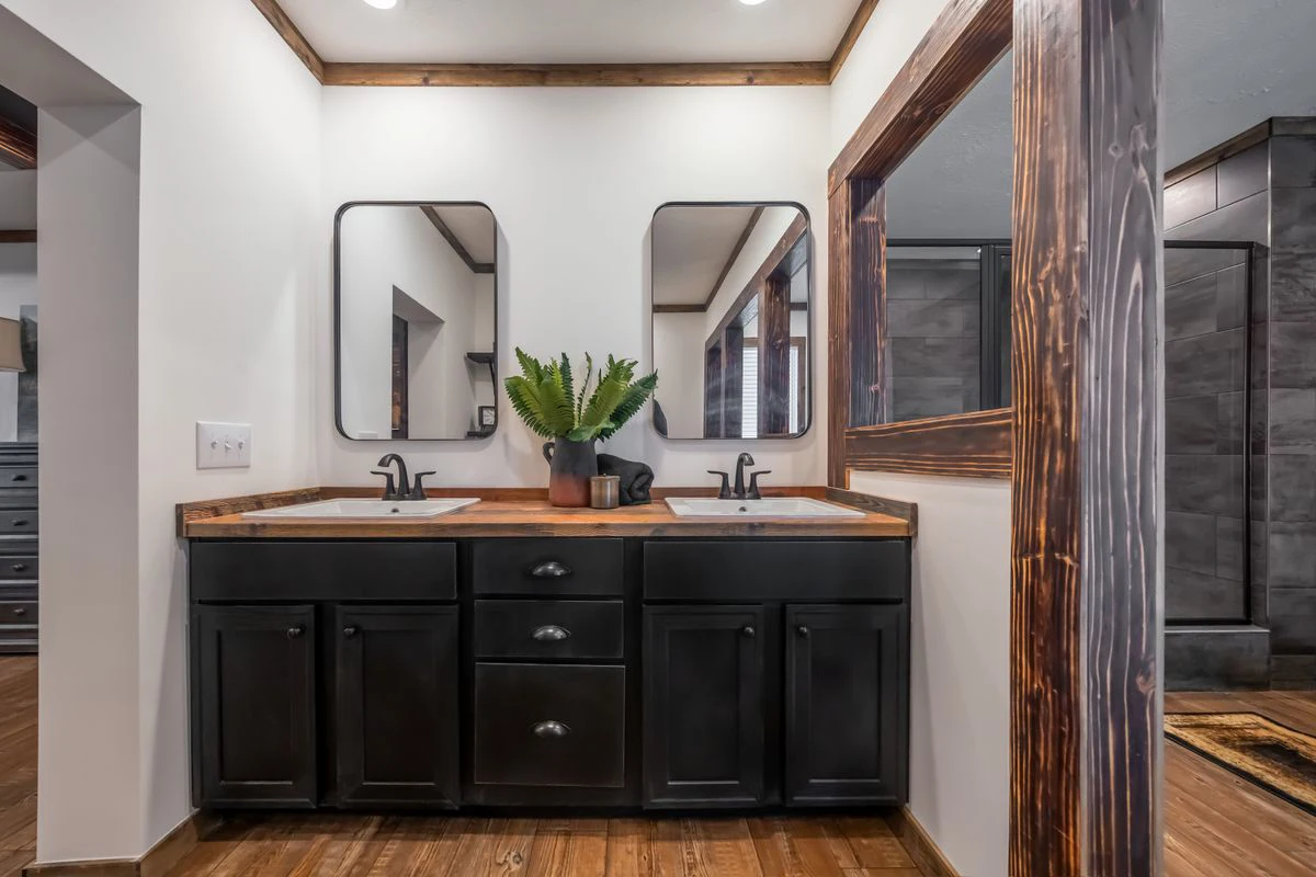 69f10235-0816-491e-b292-52b37cca88ad A double-sink bathroom vanity with black cabinets, wood countertops, two mirrors, and a potted fern in the center. The floor and trim are wood, with a walk-in shower in the background.