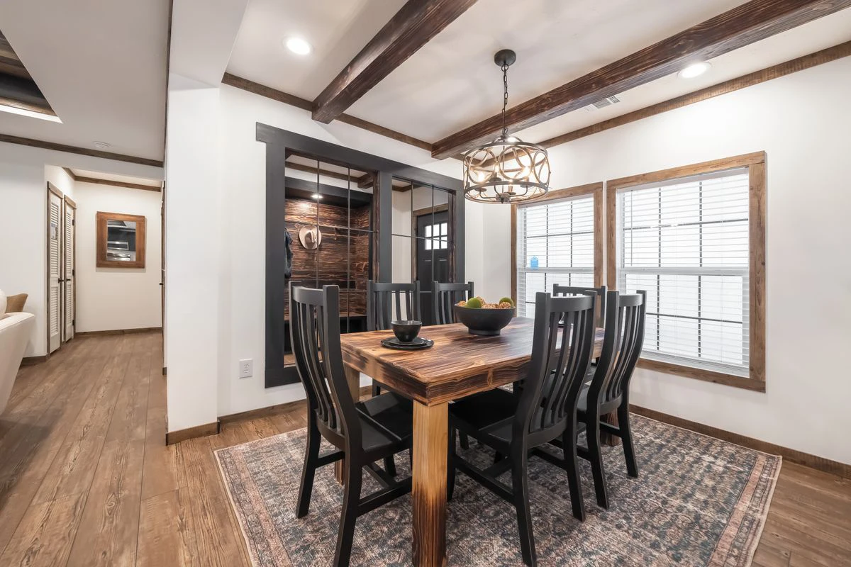 70087dda-49b3-4656-ac82-5fd88bc51699 A dining room with a wooden table, six black chairs, a patterned rug, large windows with blinds, and a modern chandelier, featuring wood accents and beamed ceiling.