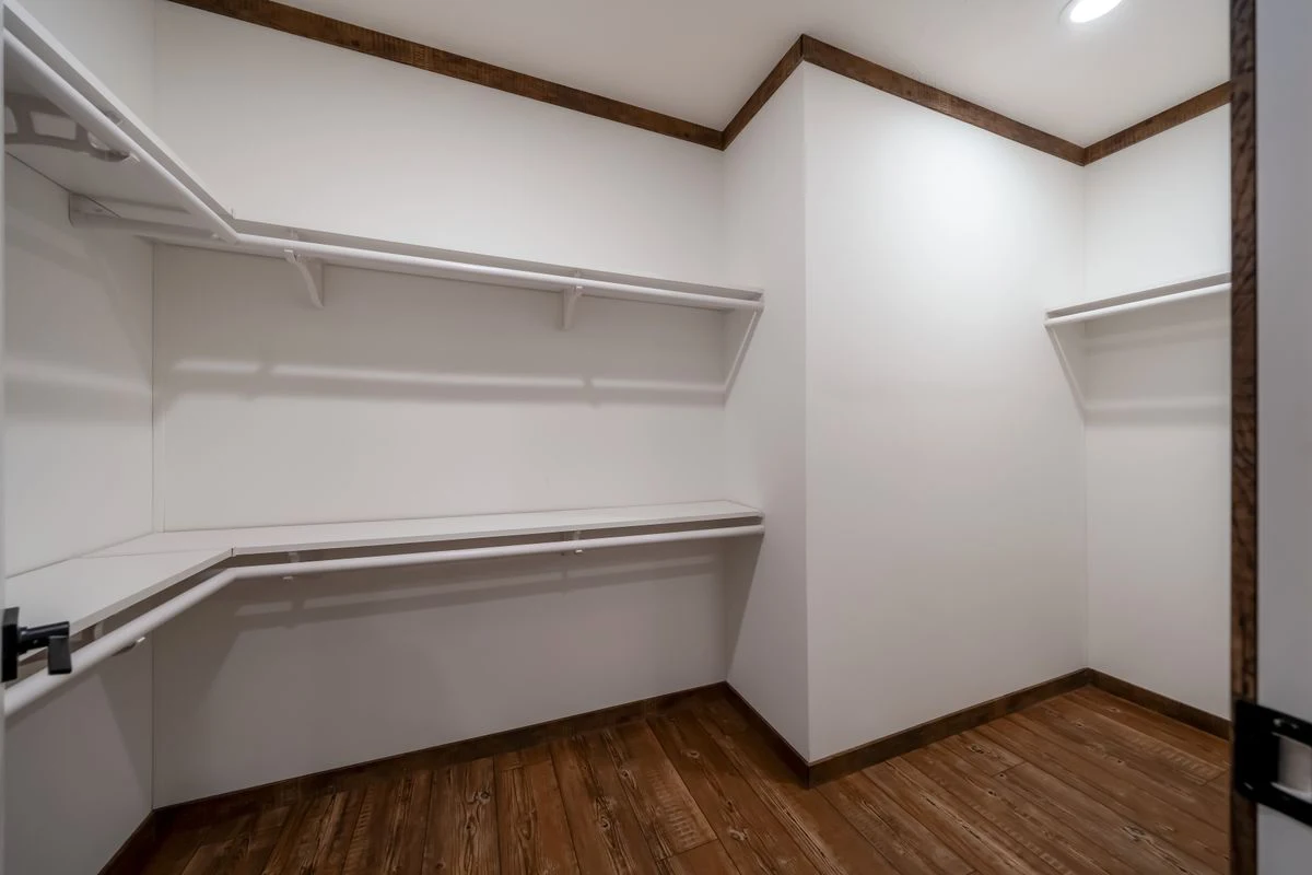 8c24dcce-decb-4f24-b4b9-81b3551e7d4c Empty walk-in closet with white shelves and wooden floor, featuring white walls and recessed ceiling lighting.