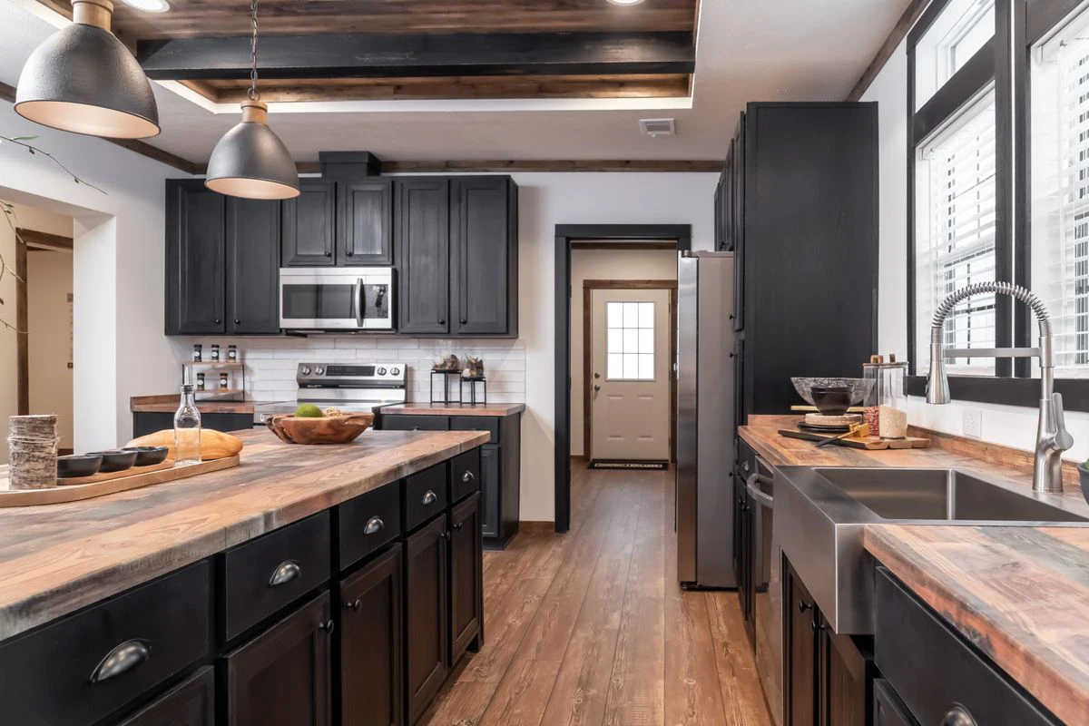 8c6bd97f-5eec-42d6-9b1f-08a9fae6bbc5 Modern kitchen with black cabinets, wood countertops, stainless steel appliances, farmhouse sink, pendant lights, and large windows letting in natural light.