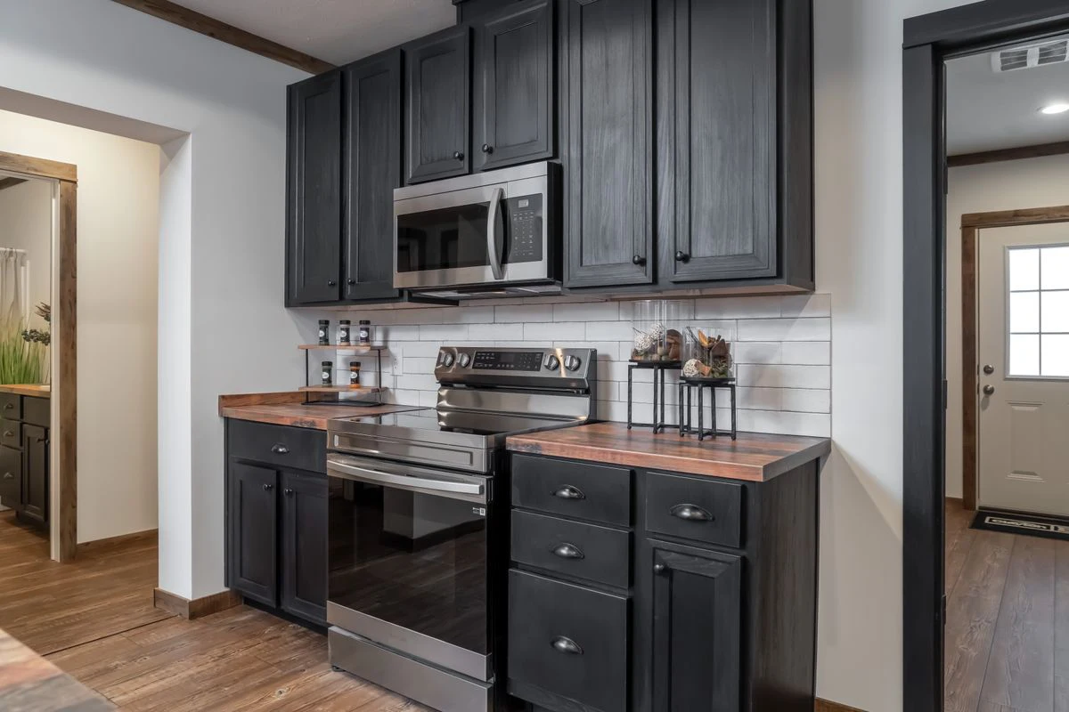 d882754c-8dee-4246-bb13-12d7b26a4394 Modern kitchen with black cabinets, stainless steel appliances, white tile backsplash, and wood countertops. The space features wooden floors and minimal decor.