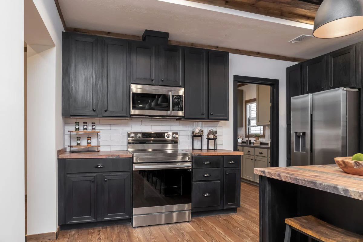 d98d606a-259e-47b2-8f7a-1e2c3e364aac Modern kitchen with black cabinets, stainless steel appliances, wood countertops, white tile backsplash, and wood flooring. Refrigerator, stove, and microwave are visible.