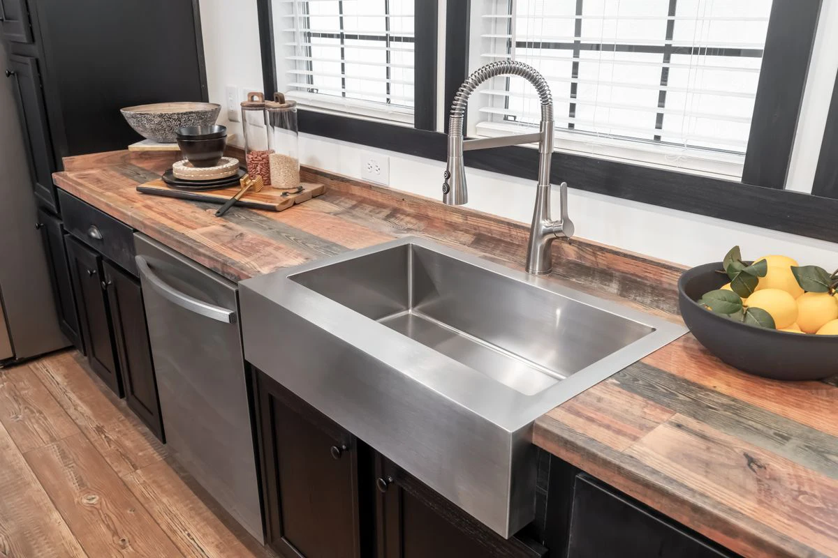 d99eaa77-da1c-495c-96b0-784762ad6c55 A modern kitchen with a stainless steel farmhouse sink, a high-arc faucet, wooden countertops, dark cabinets, and lemons in a bowl next to the sink.