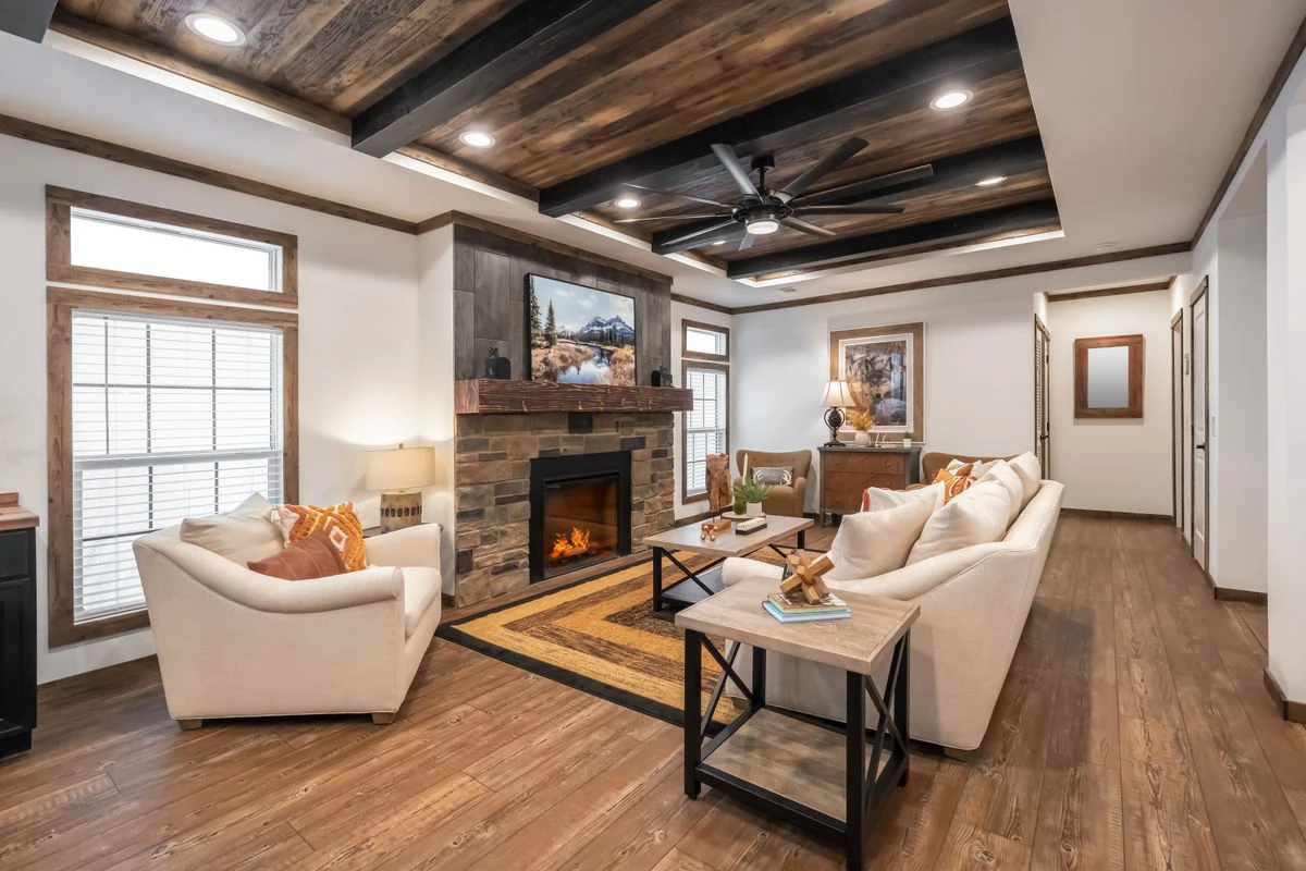 df5d8929-1431-43d0-83fd-4925543e0e95 A modern living room with wood floors, beamed ceiling, a stone fireplace, cream sofas, a coffee table, and large windows with natural light.