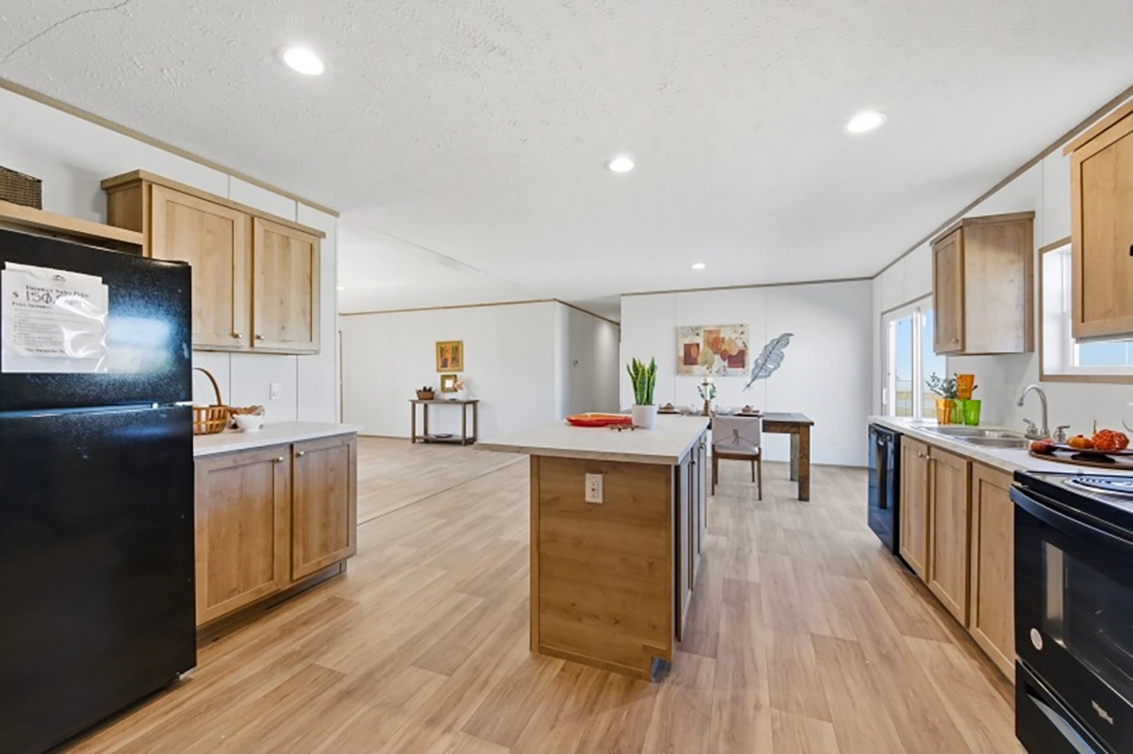 Spacious kitchen with wood cabinets, center island, black appliances, and light wood flooring, opening into a dining area with a table and chairs.