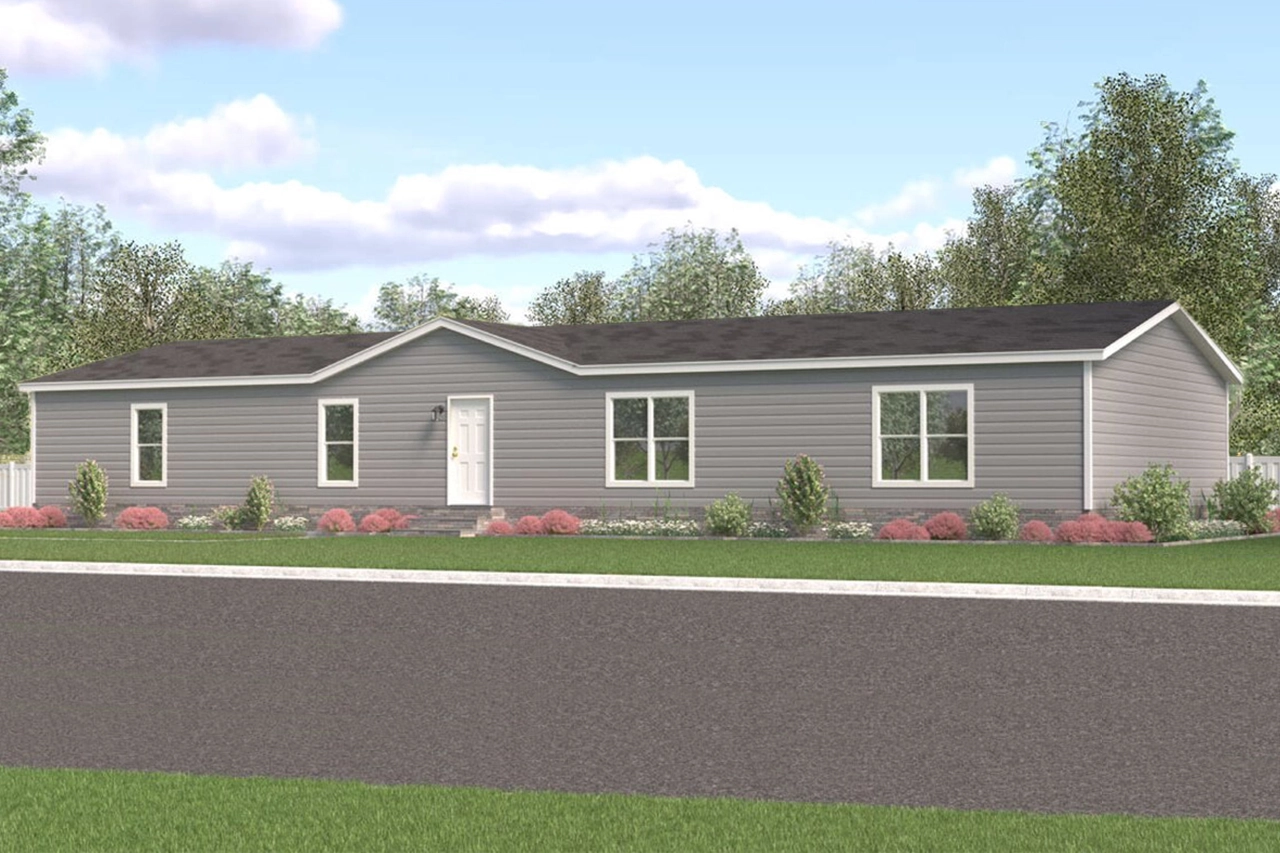 Single-story grey manufactured home with white trim, black roof, three front windows, and a white front door. The house is surrounded by landscaping and faces a paved street.