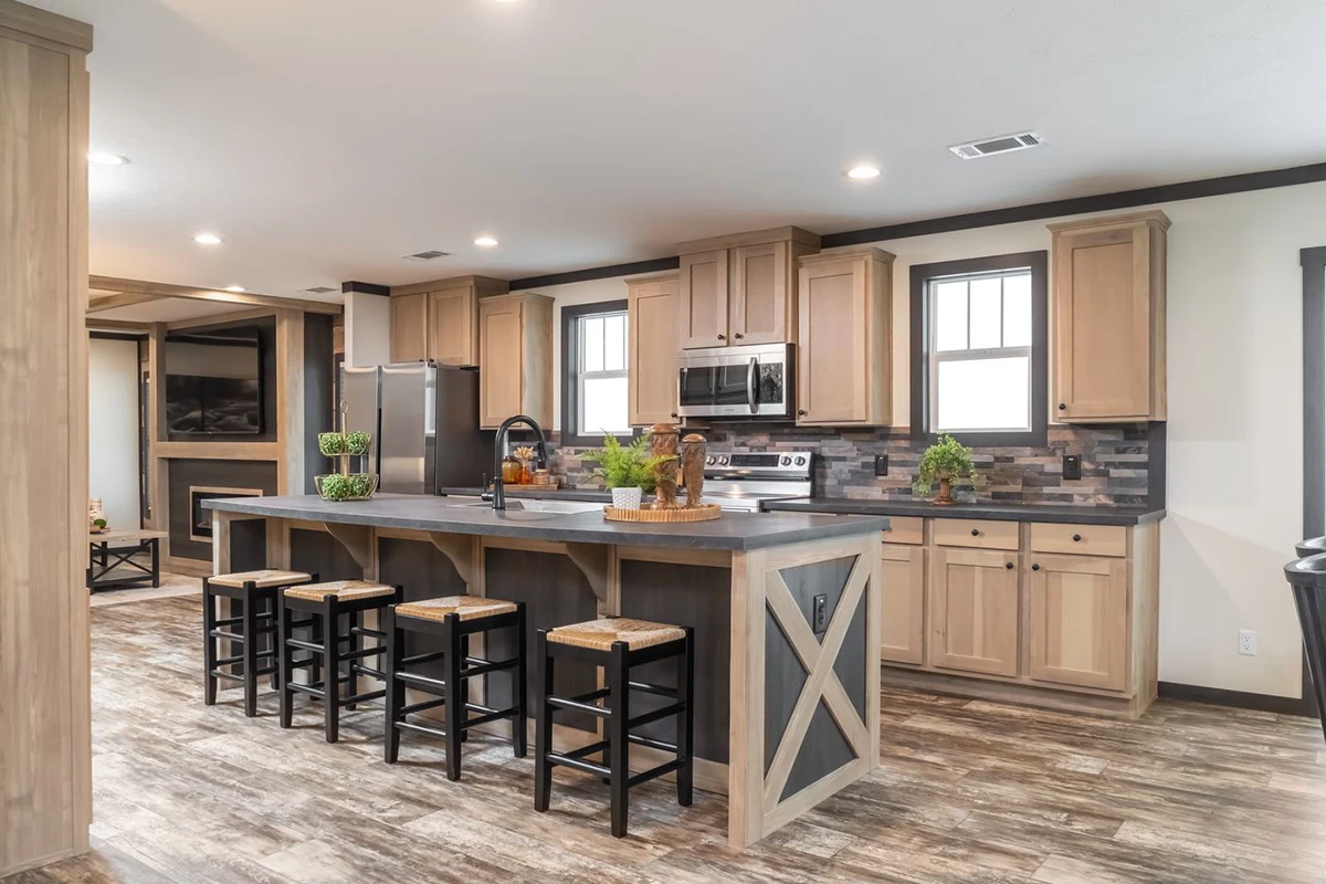 40a53541-2e16-4cfd-9125-0b2d87f4c23d Modern kitchen with wood cabinets, a large island with four bar stools, stainless steel appliances, and a tile backsplash. The floor is wood-patterned, and recessed ceiling lights are on.