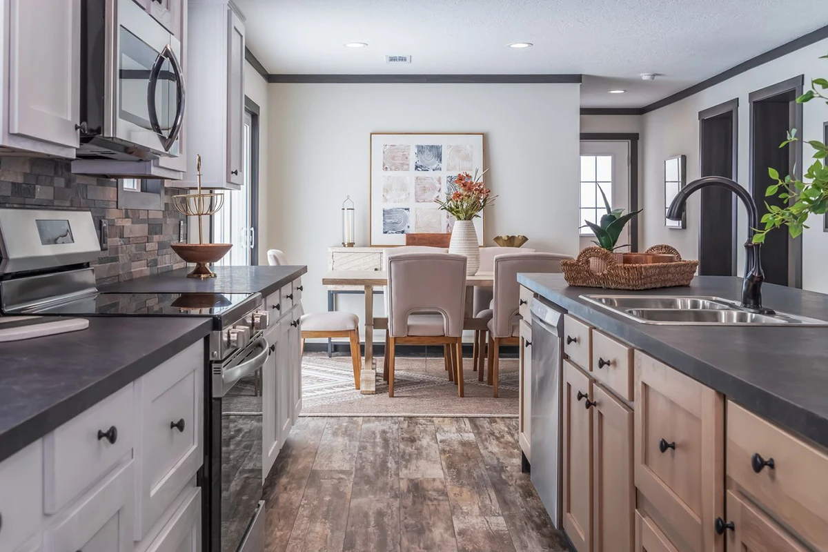 Modern kitchen with dual islands and stainless steel appliances opens into a dining area with a light wood table, upholstered chairs, and wall art. Natural light brightens the space.
