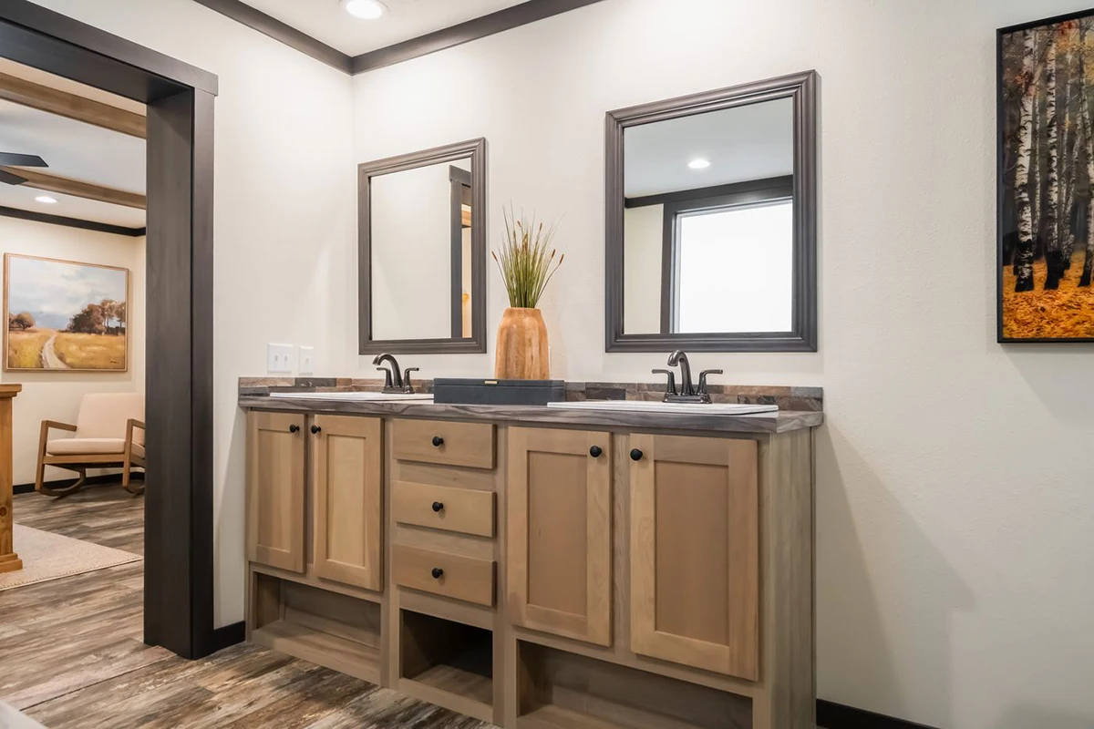 b329bcbd-d7ad-4b81-af21-3858241cf530 Bathroom with a double sink vanity, two mirrors, wooden cabinets, and a vase with tall grass on the countertop.