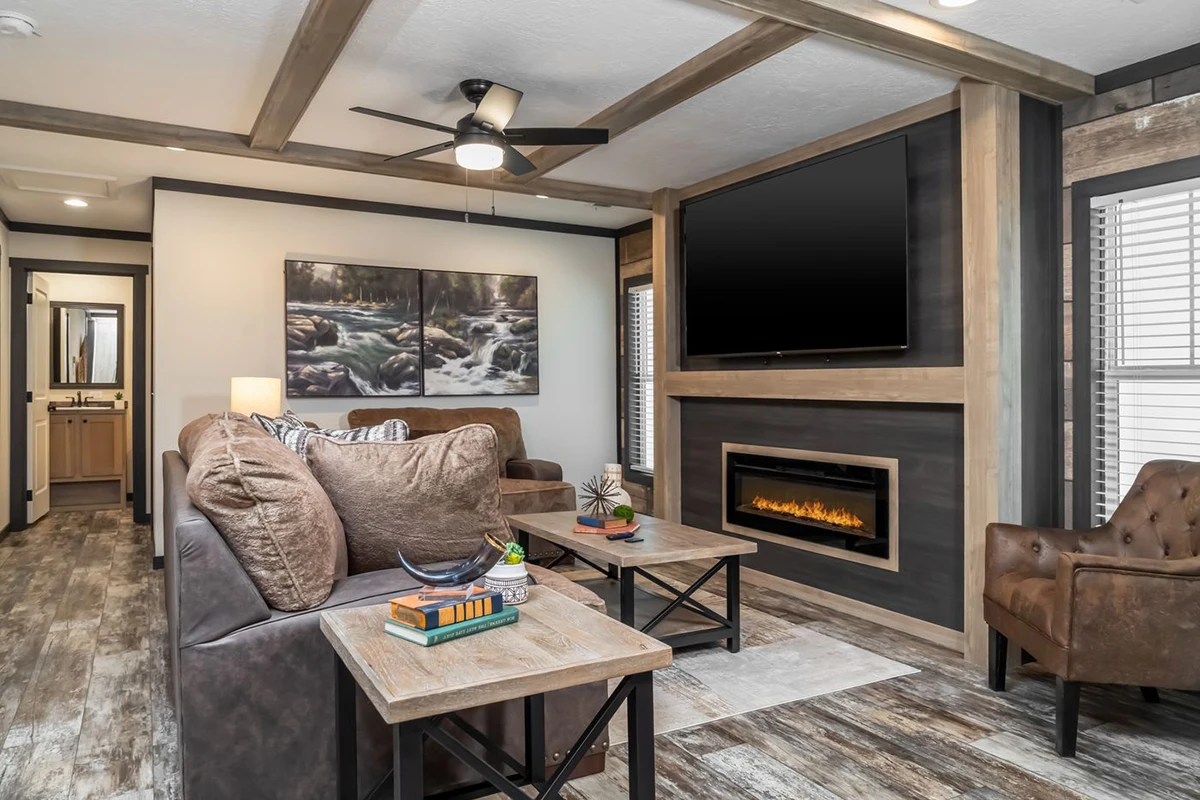 d26c8ba2-0d11-4868-8c60-fda7b2565ffe A modern living room with two brown sofas, a fireplace under a wall-mounted TV, two coffee tables, wood floors, ceiling fan, and landscape artwork on the wall.