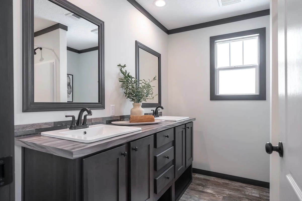 Modern bathroom with double sinks, dark wood vanity, two mirrors, a potted plant, and a window letting in natural light.