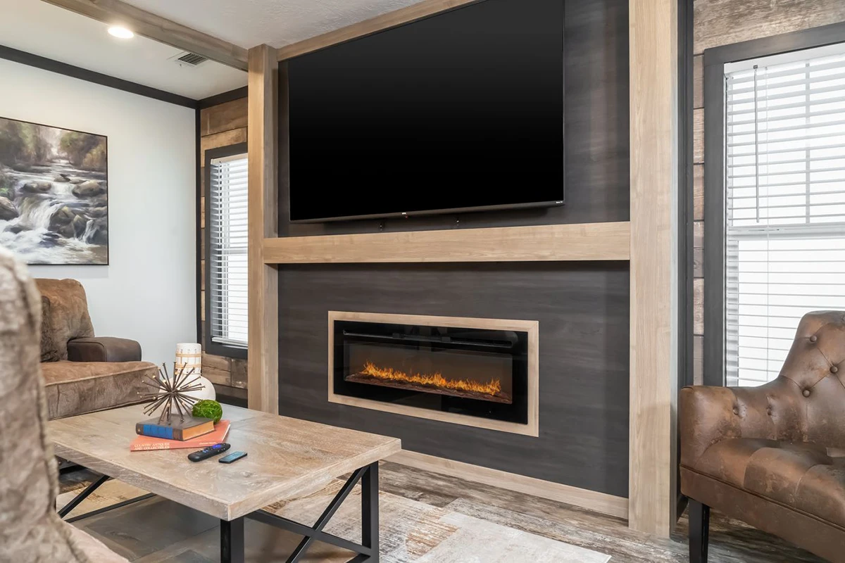 e1761c69-d611-486a-b9c5-3b9496d388d3 A modern living room with a wall-mounted TV above an electric fireplace, a coffee table with books and decor, and armchairs on either side.