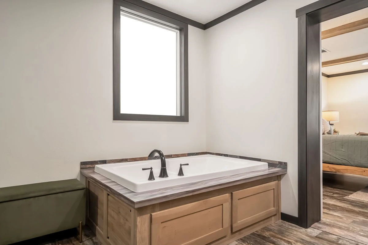 f911043f-4652-4b4e-98d4-8f7df6376226 A built-in bathtub with dark fixtures is set in a light wood frame below a window in a modern bathroom with wood-style flooring.