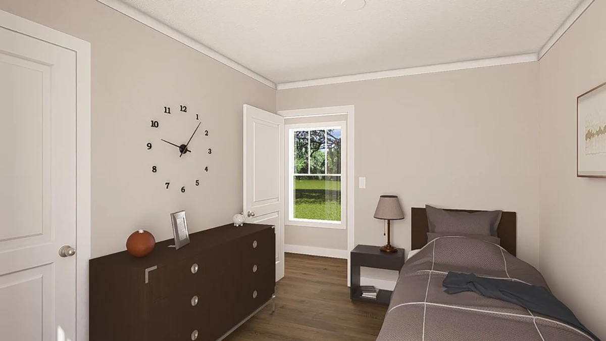 A small bedroom with a single bed, nightstand, table lamp, dresser, wall clock, framed photo, and window showing a green lawn outside.