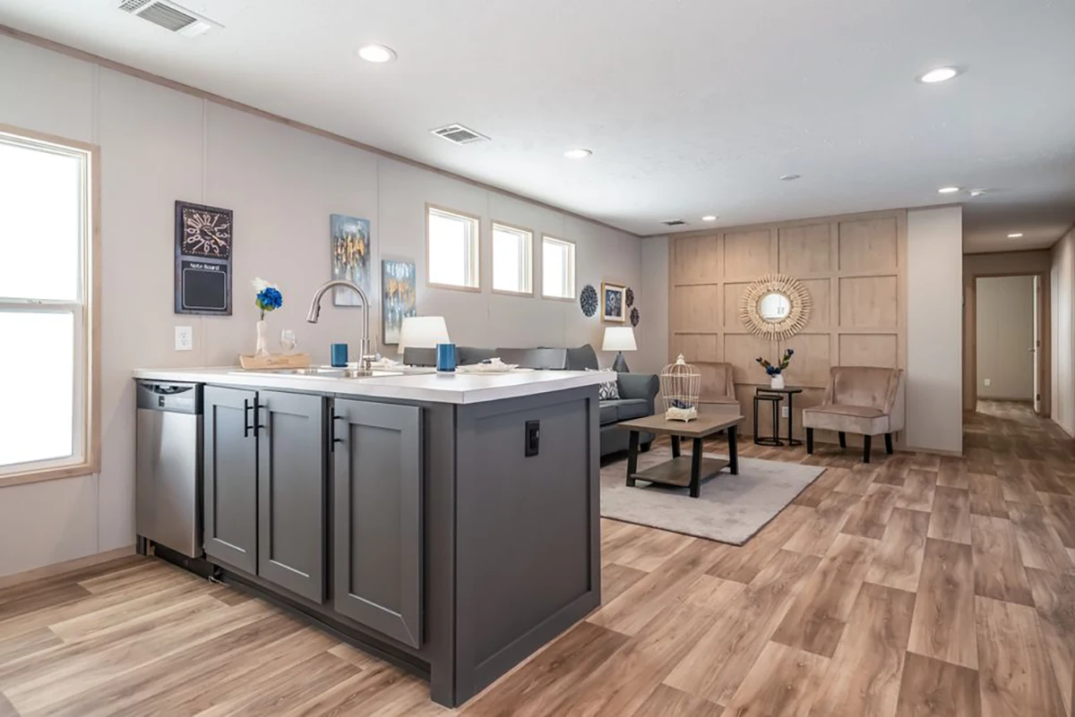 Open-plan living area with a kitchen island, gray cabinetry, wood-style flooring, a seating area with sofas and chairs, and wall art decor.