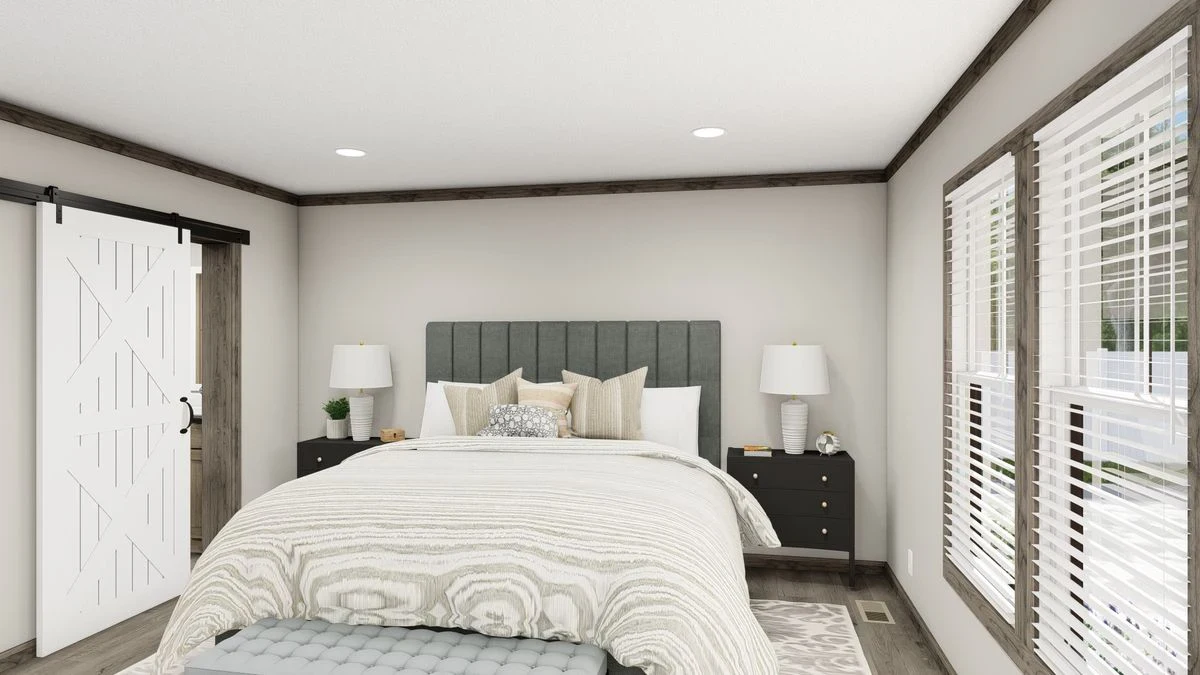 A modern bedroom with a gray upholstered bed, two black nightstands with lamps, a white barn door, and large windows with blinds letting in natural light.