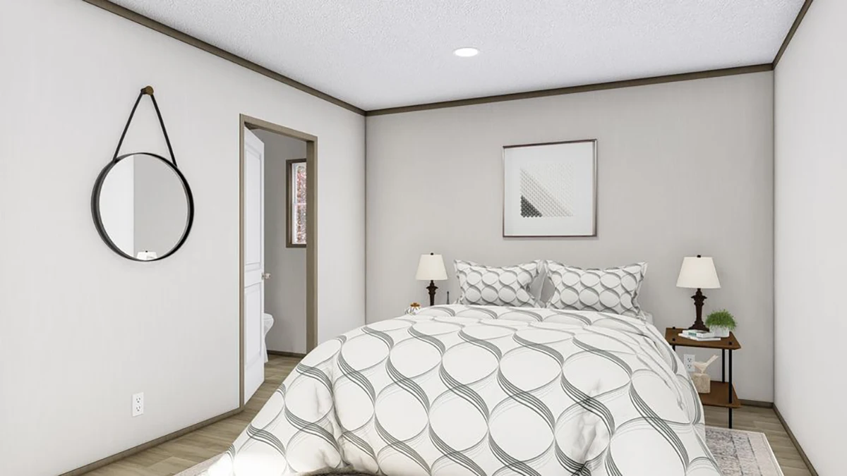 A bedroom with a neatly made bed, two bedside tables with lamps, a round mirror on the wall, and a doorway leading to a bathroom.
